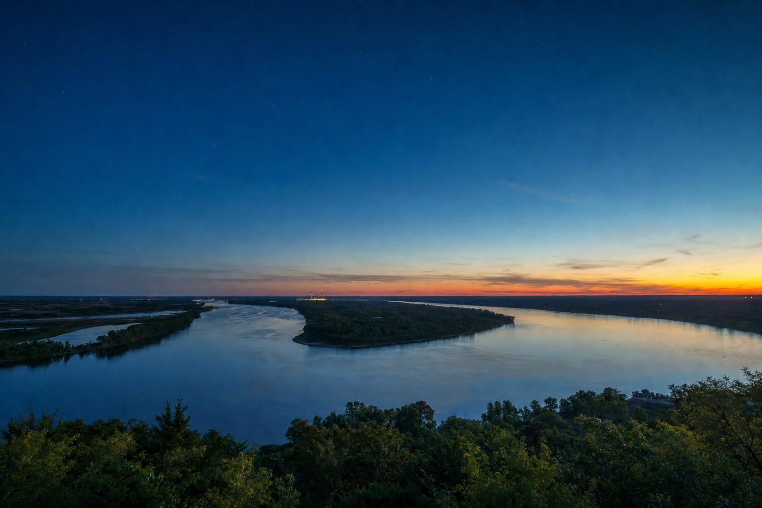 Two rivers meeting below a wooded bluff at dusk